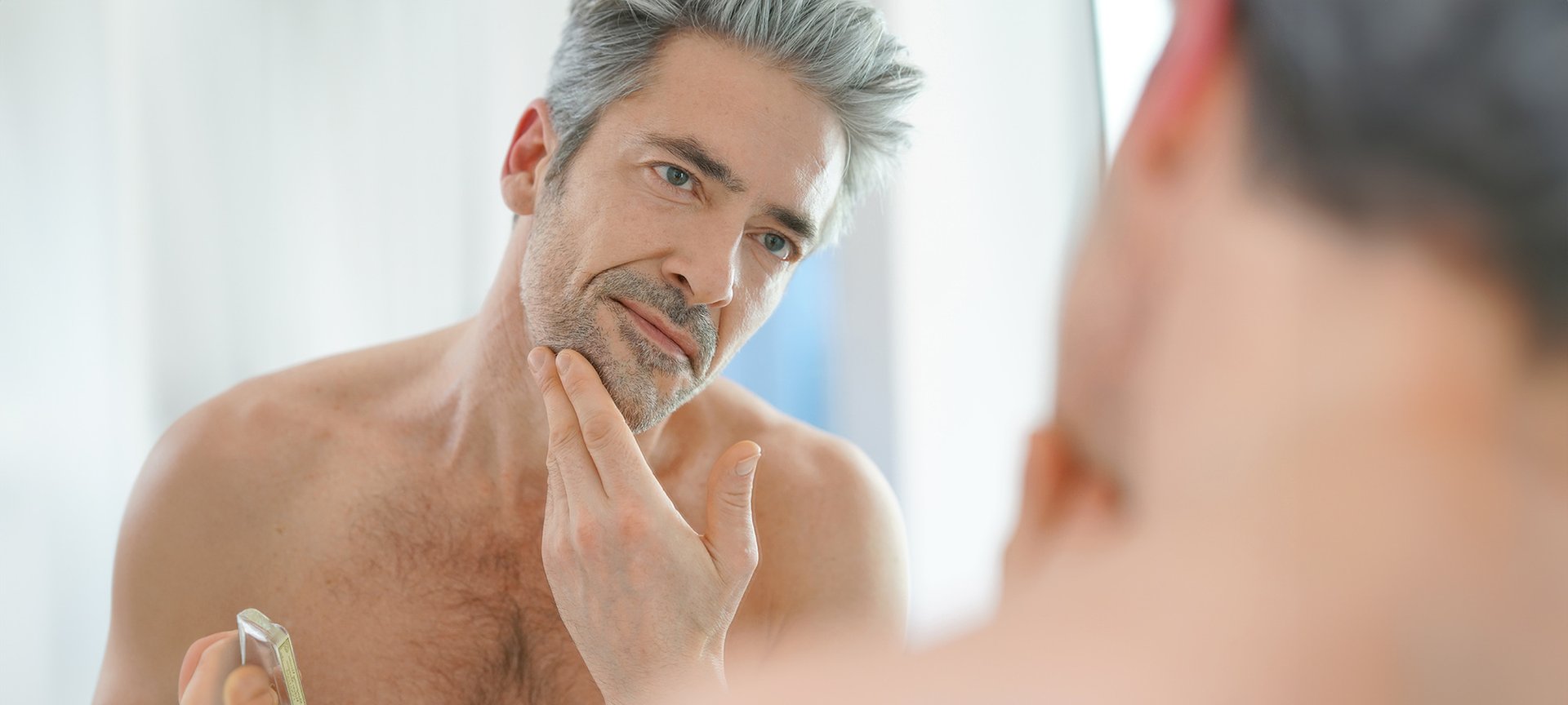mężczyzna w średnim wieku przyglądający się swojej twarzy w lustrze
