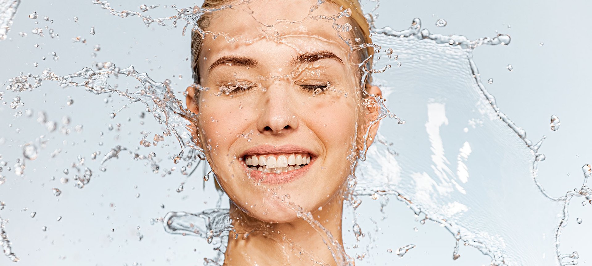 Uśmiechnięta kobiety z kroplami wody wokół twarzy przed aplikacją serum do twarzy.