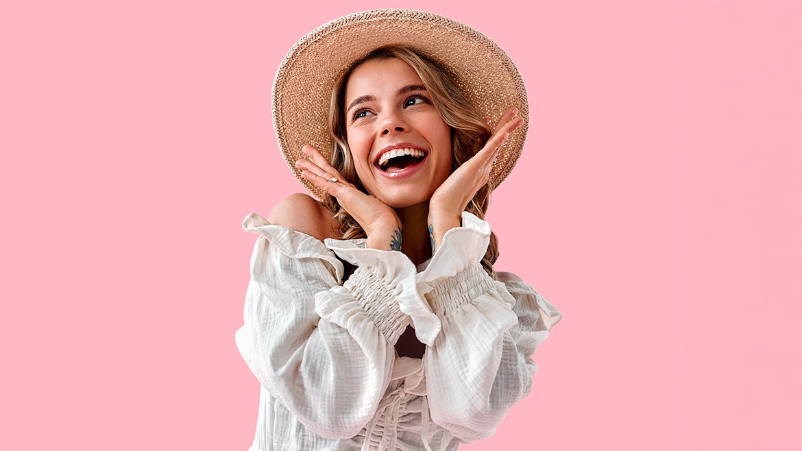 Uśmiechnięta młoda kobieta z blond włosami w kapeluszu pozuje do zdjęcia