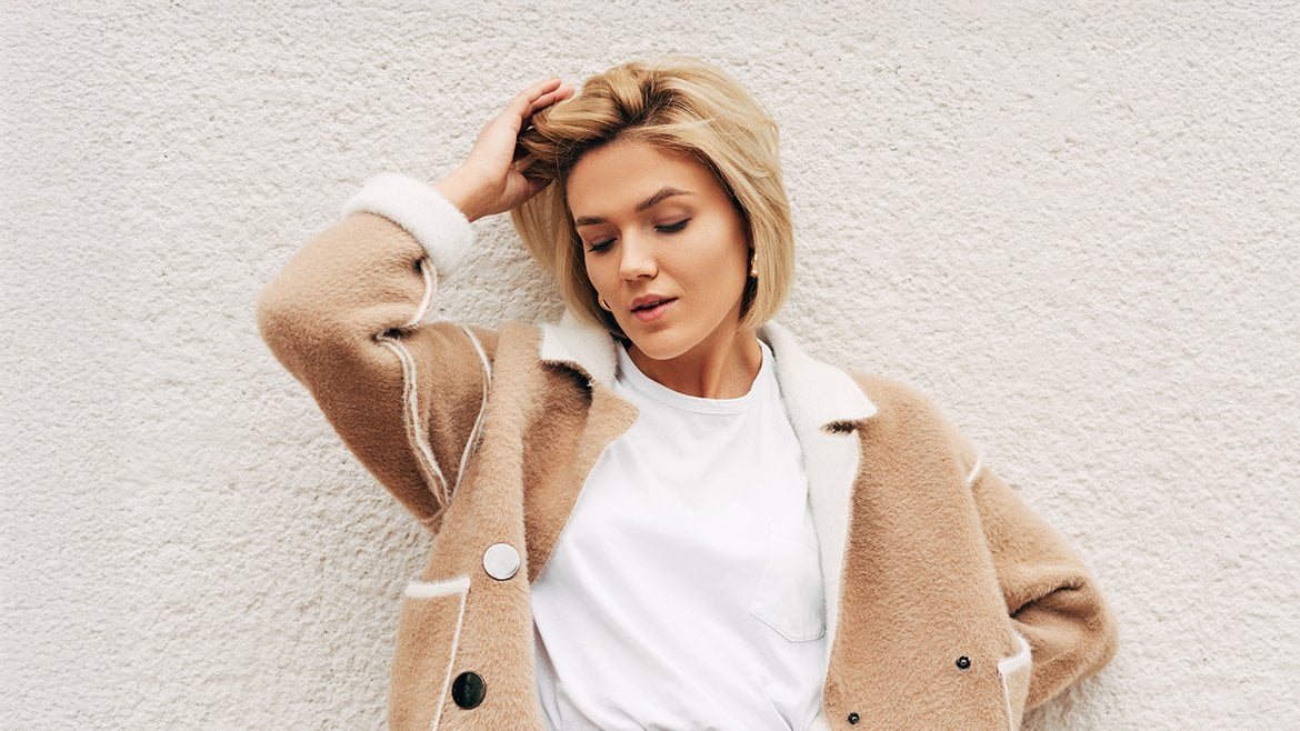 Młoda kobieta pozuje do zdjęcia i trzyma rękę na włosach w beżowym odcieniu blondu