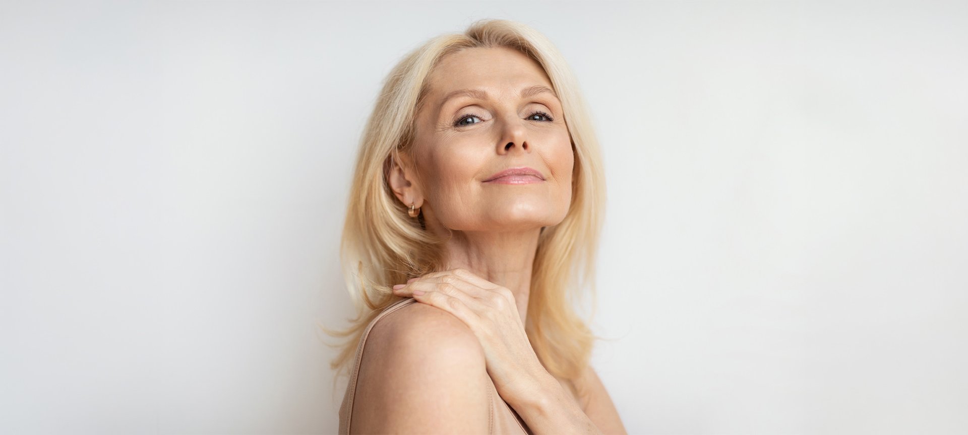 Portret kobiety w średnim wieku w blond włosach. Ma lekki, naturalny makijaż i uśmiecha się