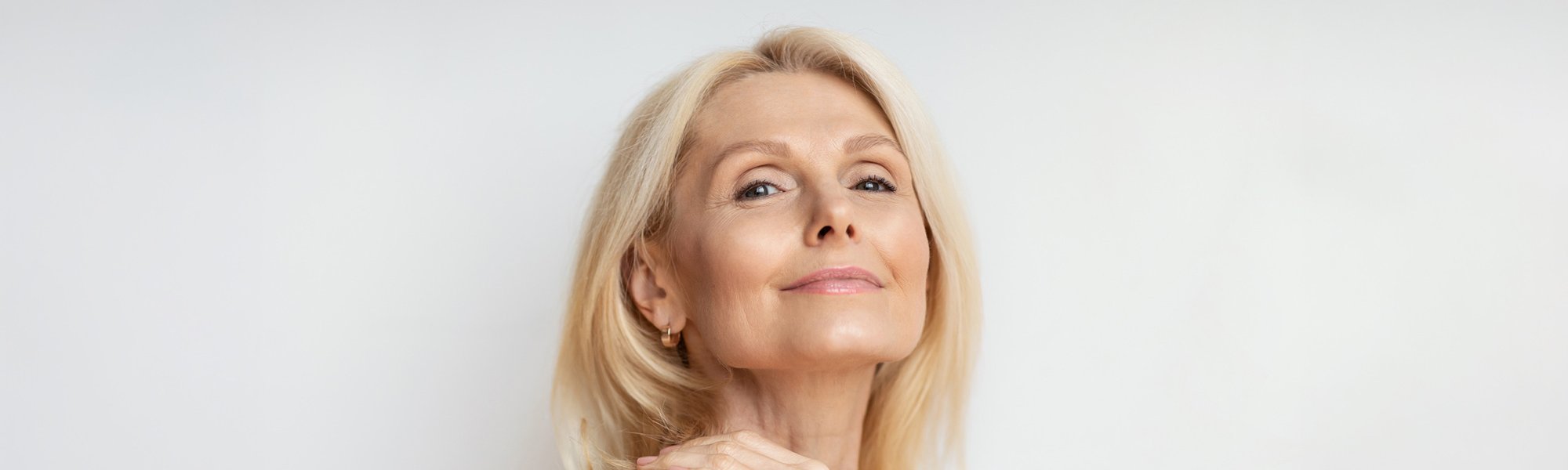 Portret kobiety w średnim wieku w blond włosach. Ma lekki, naturalny makijaż i uśmiecha się