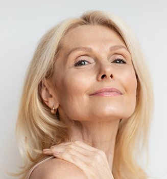 Portret kobiety w średnim wieku w blond włosach. Ma lekki, naturalny makijaż i uśmiecha się
