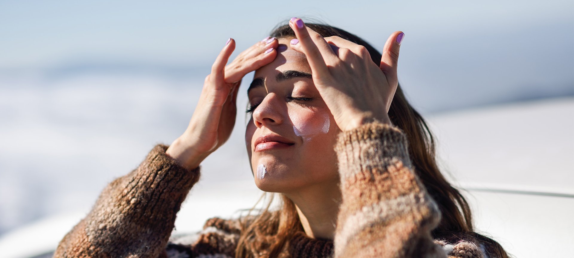  kobieta w zimowej aurze nakładająca na twarz krem SPF50