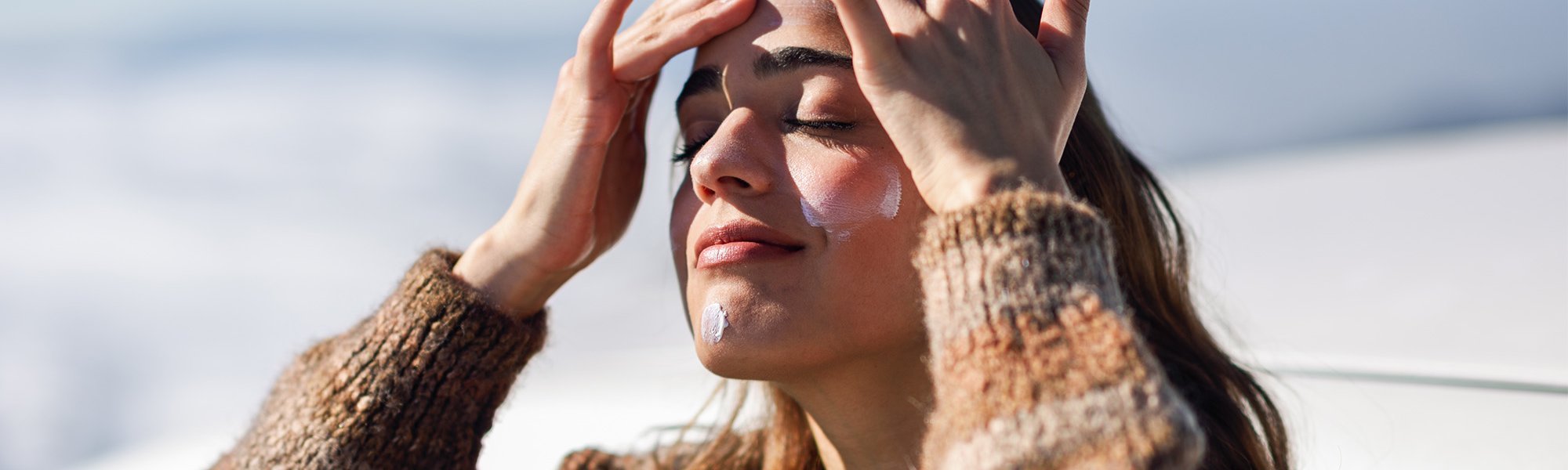 kobieta w zimowej aurze nakładająca na twarz krem SPF50