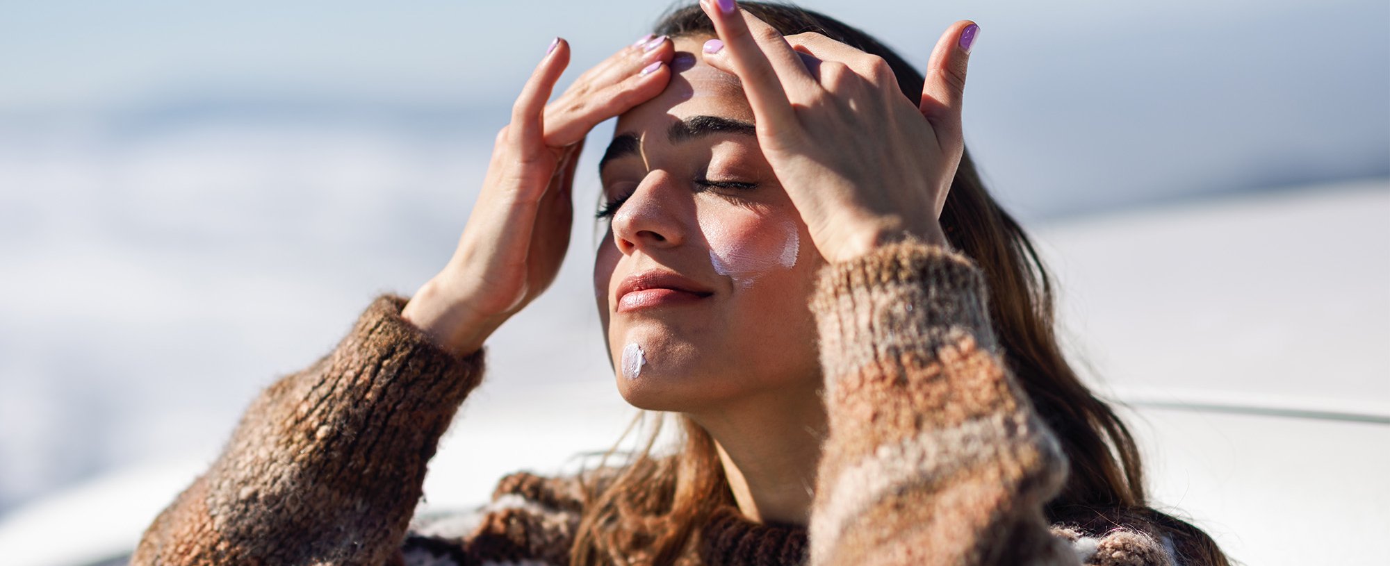 kobieta w zimowej aurze nakładająca na twarz krem SPF50