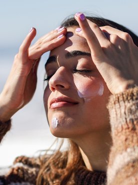 kobieta w zimowej aurze nakładająca na twarz krem SPF50